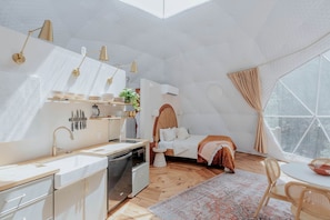 Een compacte, moderne slaapkamer met een groot raam, een kleine kitchenette en een gezellige zithoek.