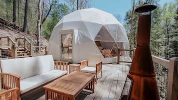 Een geodetische koepelstructuur met een houten terras, tuinmeubilair en een schoorsteen.