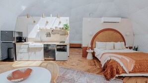 Una habitación compacta y moderna, con kitchenette, una cama con cabecera de madera y una mesita auxiliar pequeña.