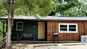A rustic cabin with a green door, a bench, and a mailbox.