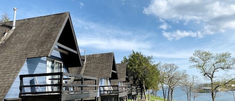Une rangée de chalets en bois dotés de balcons, une zone herbeuse et un lac en arrière-plan.