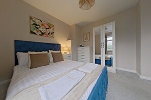 A bedroom with a large bed, a dresser, a mirror, and a painting on the wall. - Toast Stays - Hydenside House (Consett)