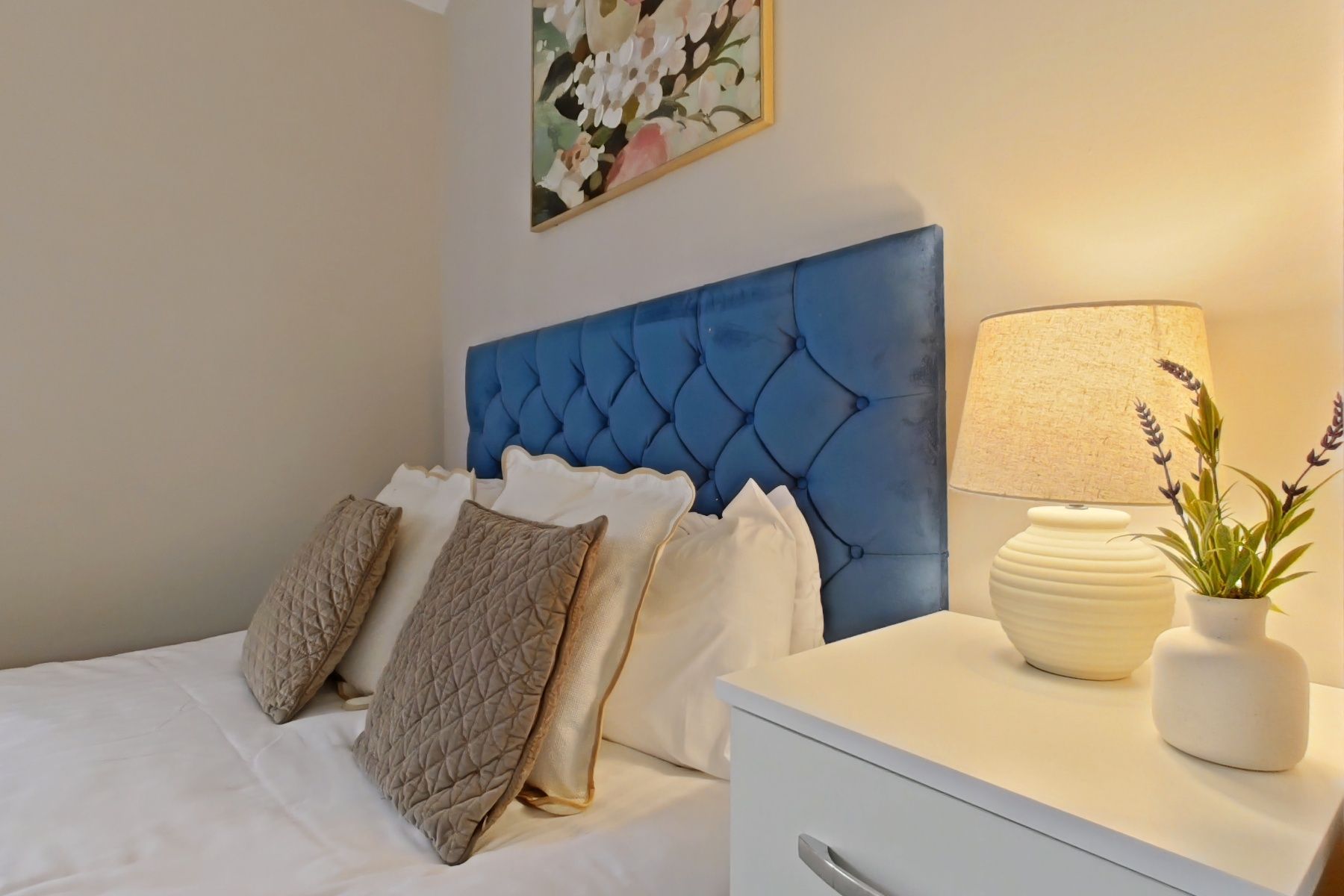 Une chambre à coucher avec une tête de lit capitonnée, une table de chevet avec une lampe et des coussins décoratifs.