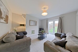 A modern living room with two sofas, a coffee table, a TV, and a large window with curtains. - Toast Stays - Hydenside House (Consett)
