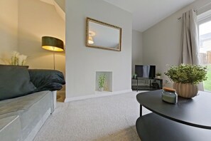 A living room with a sofa, a lamp, a television, a small table with a plant, and a mirror on the wall. - Toast Stays - Hydenside House (Consett)