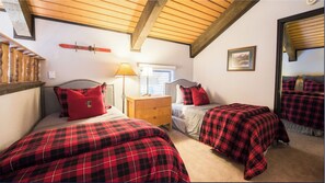 A bedroom with two beds, each with red and black plaid bedding, a wooden dresser, a nightstand, and a window with blinds. - Ski In-Out Condo in the "Heart of Mt. Crested Butte" w/ Ski Locker (Mount Crested Butte)