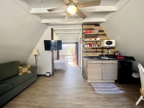 Ein Loft-Zimmer mit Küchenzeile, einer Couch, einem Fernseher und einem Deckenventilator.