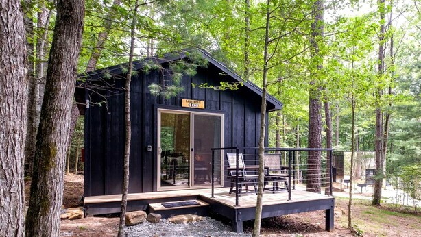 Een chalet met een terras, een bord met de tekst 'Lazy Bear Lodge' en een grindpad dat naar de ingang leidt.