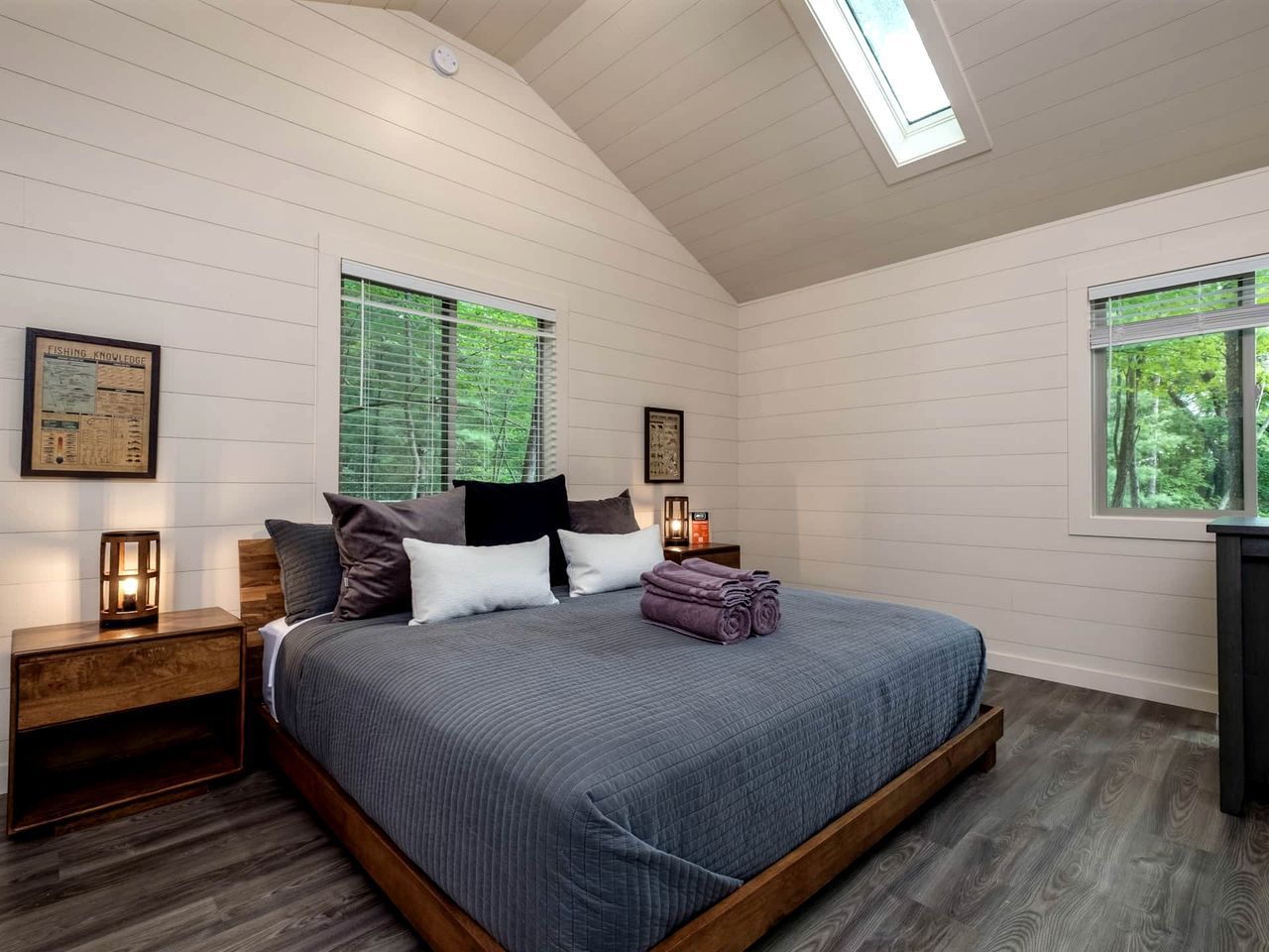 Ein Schlafzimmer mit einem großen Bett, einem Holzkopfende, zwei Nachttischen, einem Fenster mit Jalousien und einem Oberlicht.