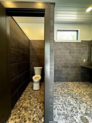 Un baño con inodoro, ventana y zona de ducha con piso de diseño de guijarros.