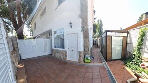 Un patio con suelo de baldosas, una puerta blanca y una pequeña estructura de vidrio.