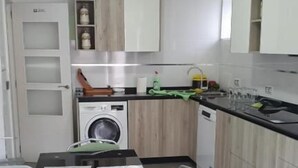 Una cocina moderna con armarios blancos, una mesa de comedor roja y una lavadora.