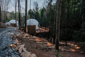Metsässä sijaitsee kaksi kupolimaisia mökkiä, jotka on yhdistetty toisiinsa puinen terassi, jossa on kivestä tehdyt portaat.