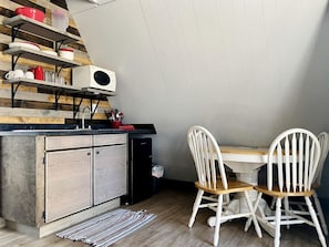 Eine Küche mit Holzregalen, einem Kühlschrank, einer Mikrowelle und einem Essbereich mit weißen Stühlen und einem Tisch.