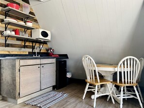 A kitchen with wooden shelves, a microwave, and a dining area with white chairs. - Family Glamping Getaway with Amazing Lake Views of Table Rock Lake (Branson)