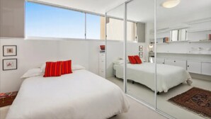 A modern bedroom with a large bed, a mirror, and a view of the sky. - Beachside Paradise - Ocean Views, Central Position (Sydney)