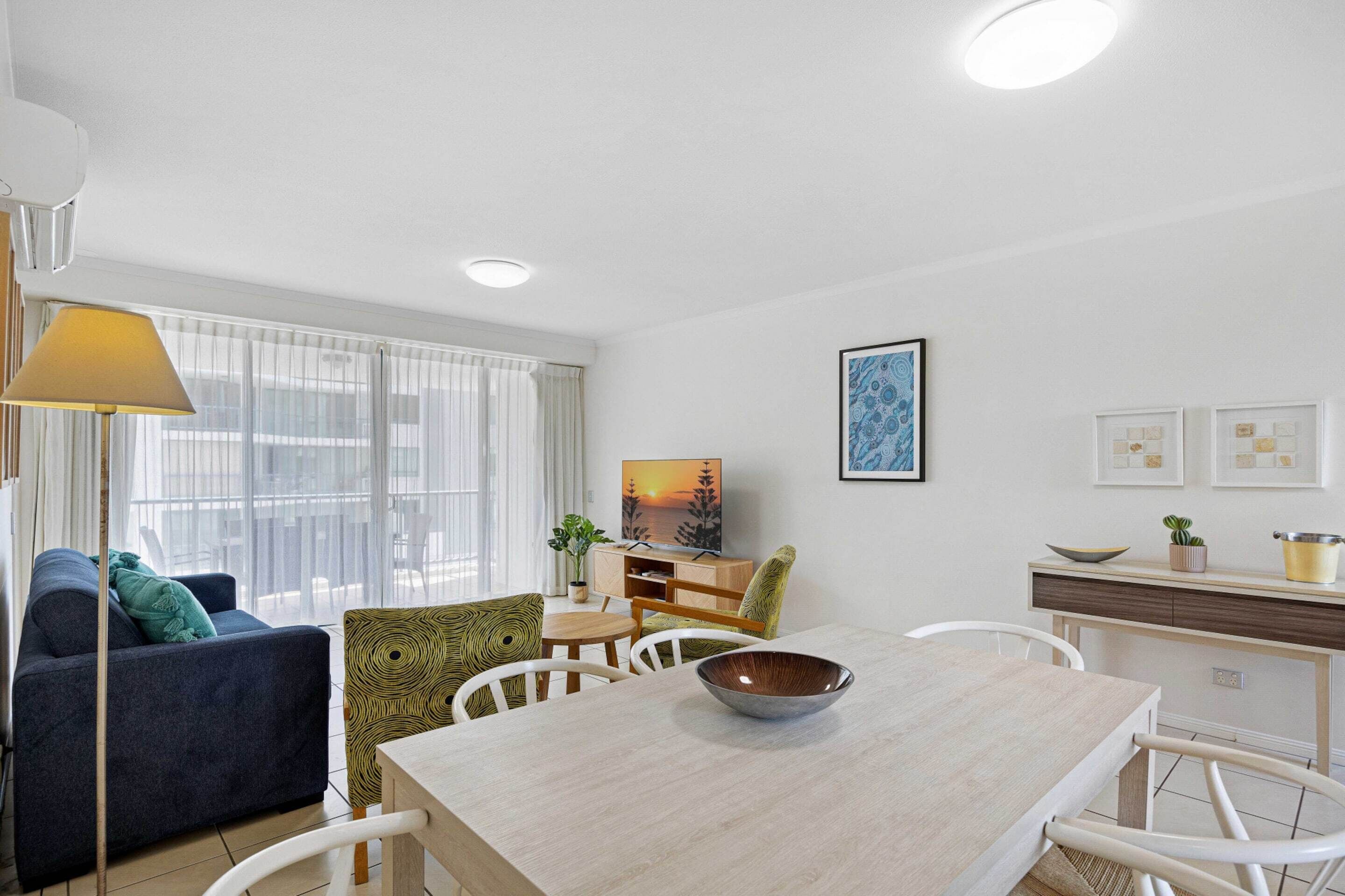 A modern living room with a dining area, featuring a sofa, chairs, a table, and a TV.