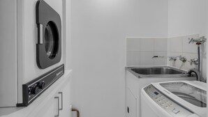 A modern laundry room with a front-loading washer and dryer, a stainless steel sink, and a control panel. - Bright 1-bed Unit With Balcony in Central Adelaide (Adelaide)