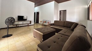 Ein modernes Wohnzimmer mit einem Ecksofa, einem Flachbildfernseher, einem Standventilator und einer Holzzahl.