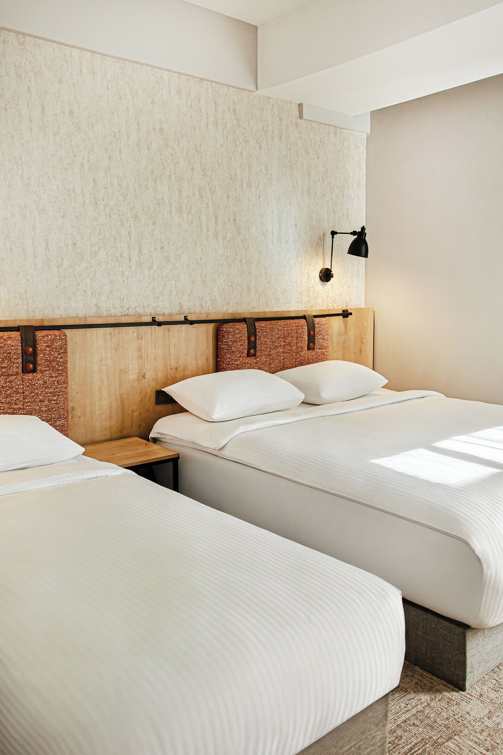 A hotel room with two beds, wooden headboards, a textured wall, and a bedside lamp.