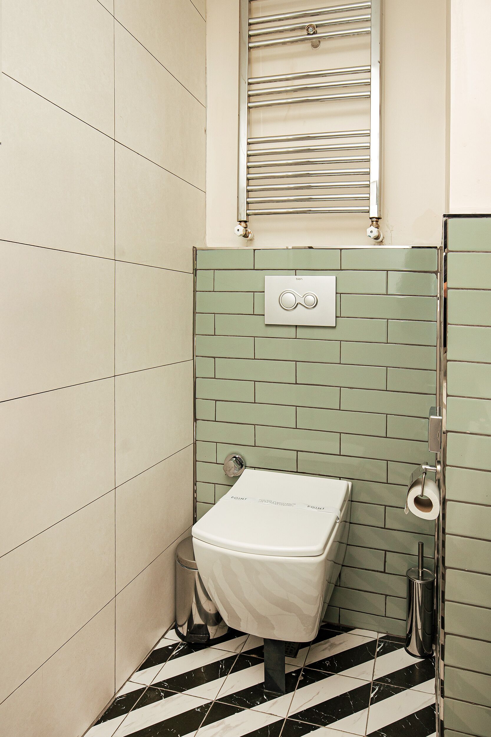 A bathroom with a toilet, a trash bin, a towel rack, and a toilet paper holder.