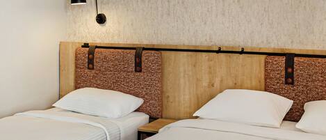 Une chambre d’hôtel avec deux lits simples, une tête de lit en bois, un mur à texture et une petite table de chevet avec une lampe.
