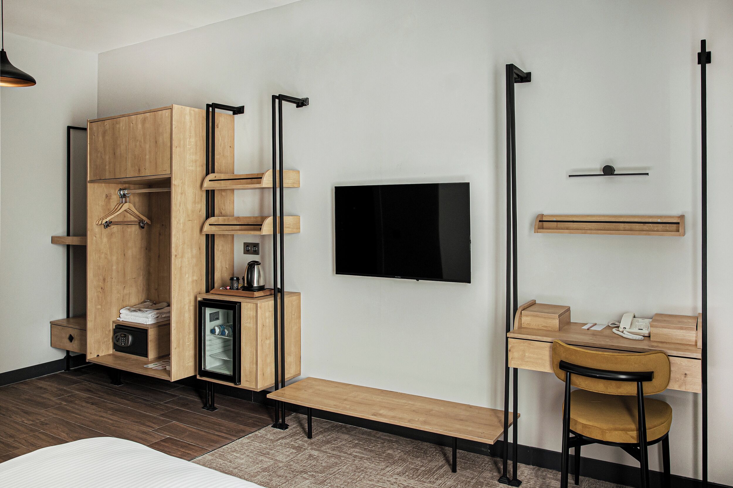 Una habitación de hotel compacta con un armario de madera, un escritorio con una silla, un televisor y un refrigerador pequeño.