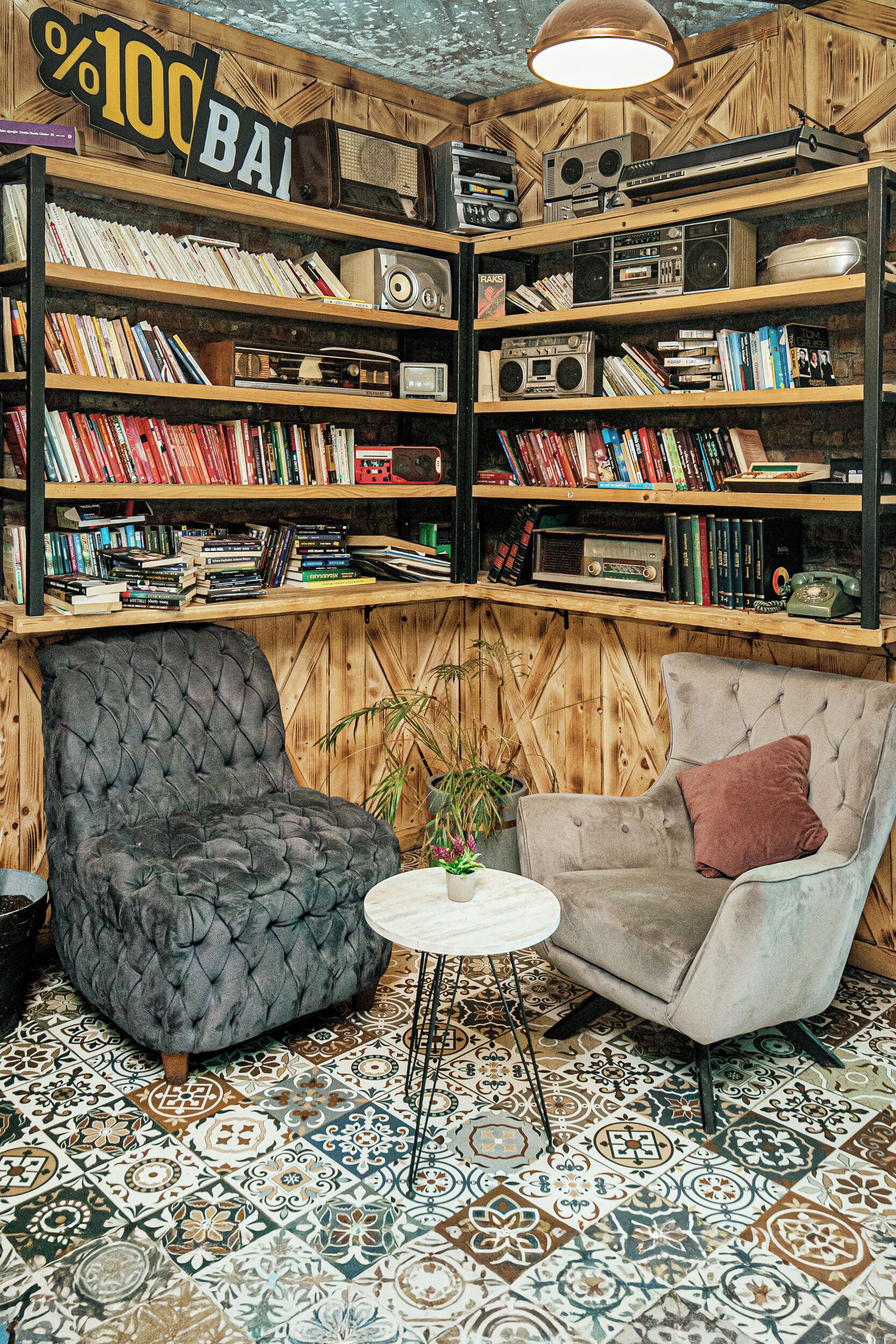 A cozy room with a bookshelf filled with books and audio equipment, two plush armchairs, a small round table, and a patterned floor.