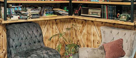 A cozy room with a bookshelf filled with books and audio equipment, two plush armchairs, a small round table, and a patterned floor.