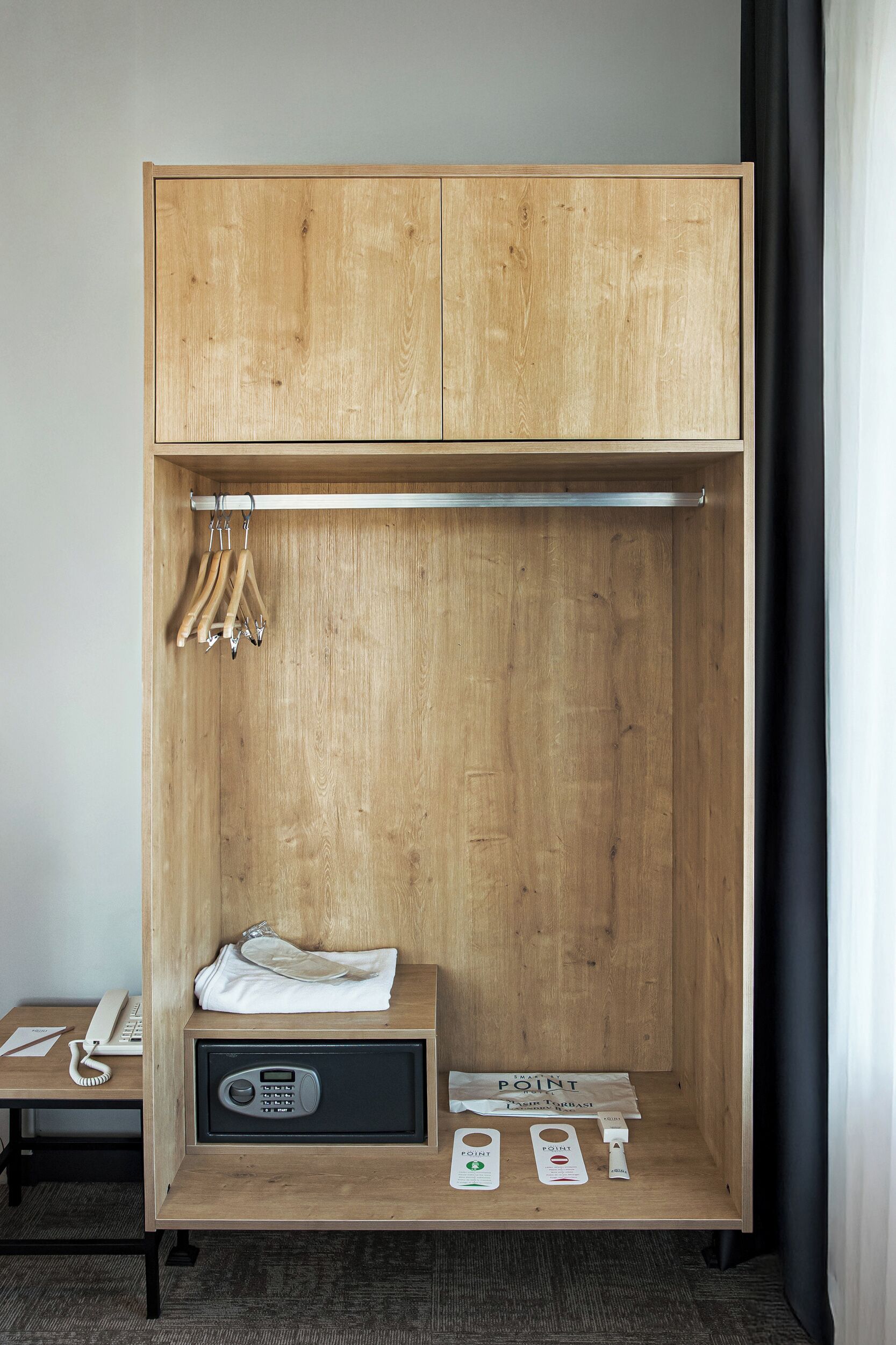 A wooden wardrobe with a hanging rack, a small shelf with a radio, and a desk with a telephone and a notepad.