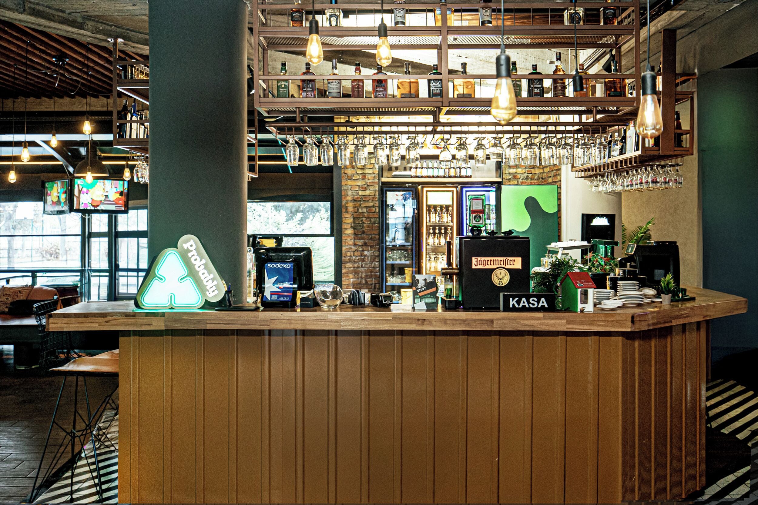 Eine Bar mit Holztresen, Flaschenregalen, hängenden Glühbirnen und einem Fernsehbildschirm.