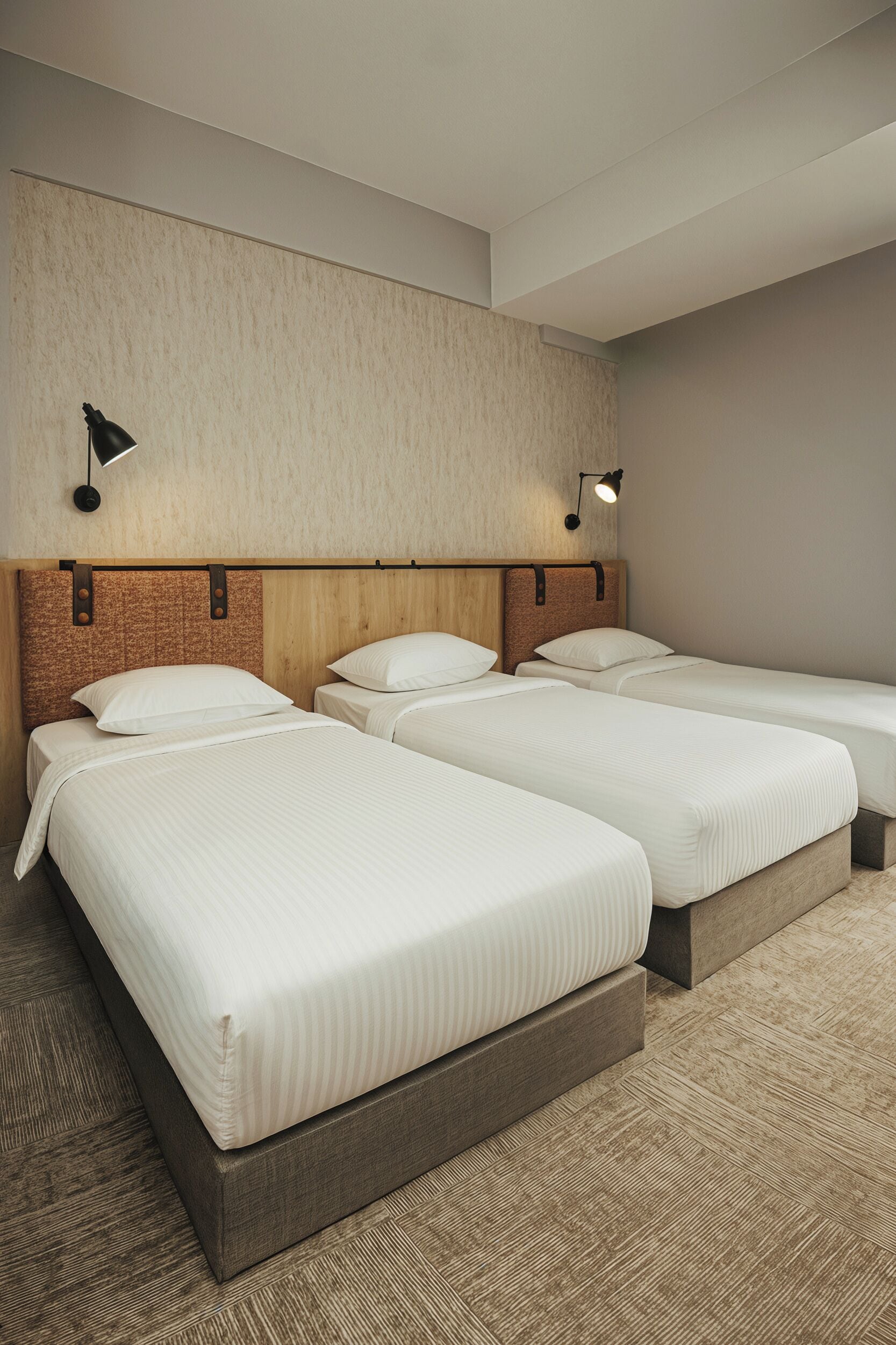 A hotel room with three single beds, a wooden headboard, and two wall-mounted lamps.