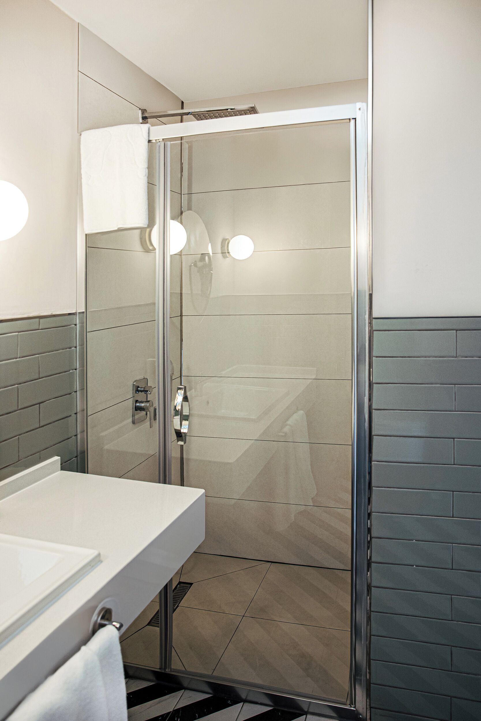 A modern bathroom with a glass shower enclosure, a white sink, and a mirror.