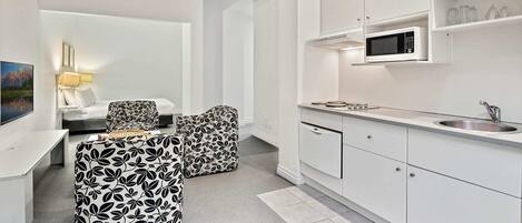 A modern kitchen with white cabinets, a microwave, and a sink. There is a dining area with a table and chairs.