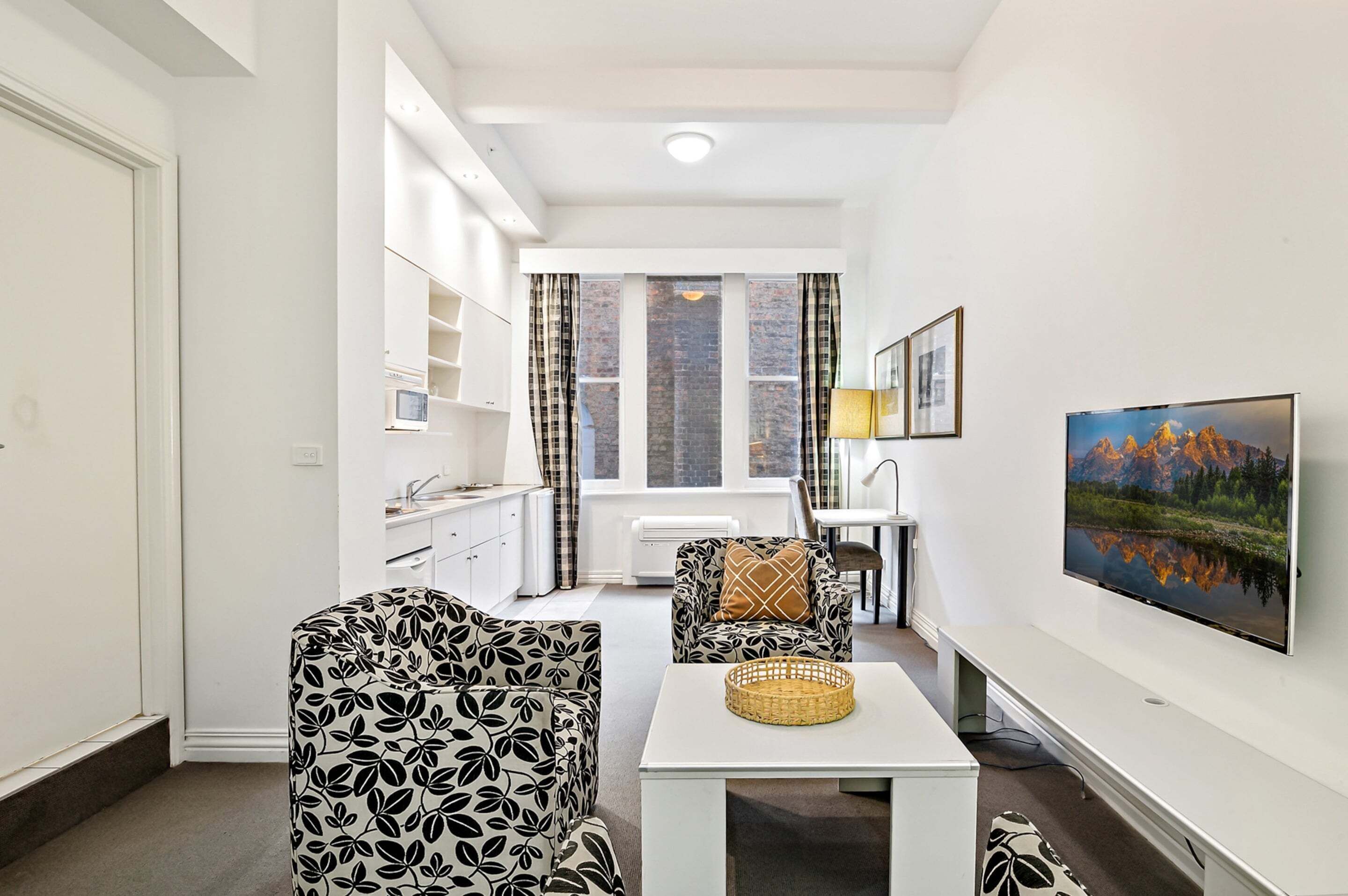 Un salon moderne avec un canapé blanc, une table basse et un téléviseur. Il y a une fenêtre avec des rideaux et un tableau accroché au mur.