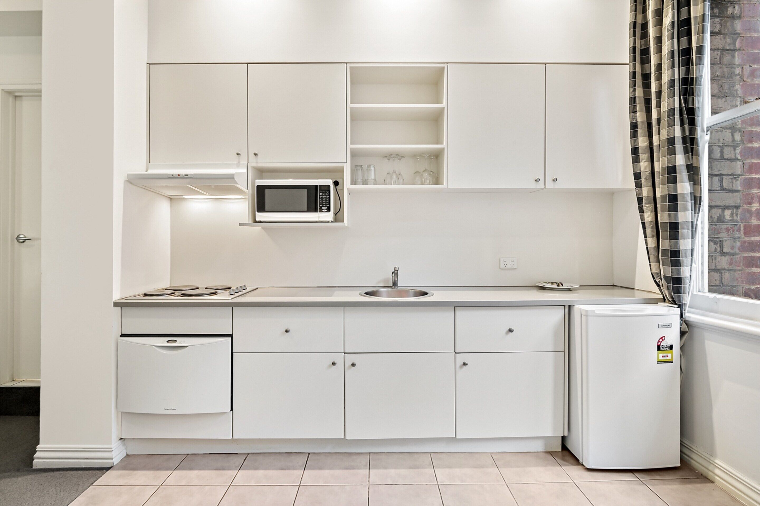 Une cuisine moderne avec des meubles blancs, un four à micro-ondes encastré, un évier et un réfrigérateur.