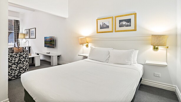Ein Hotelzimmer mit einem großen Bett, zwei Nachttischlampen, einem Schreibtisch, einem Stuhl und zwei gerahmten Bildern an der Wand.