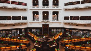 Eine großzügige Bibliothek mit mehreren Ebenen Bücherregale, einem zentralen Lesebereich und einer imposanten Treppe.