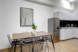 A modern kitchen with white cabinets, a stainless steel refrigerator, and a dining area with a wooden table and wire mesh chairs. - Spacious apartement 1BDR/6P - Proche Opéra (Paris)