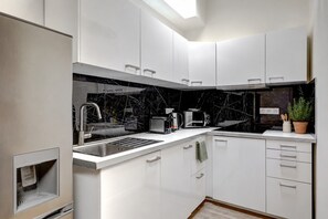 A modern kitchen with white cabinets, a black marble backsplash, and stainless steel appliances. - Grand 1BDR/6P – Gare de l'Est / Canal Saint-Martin (Paris)