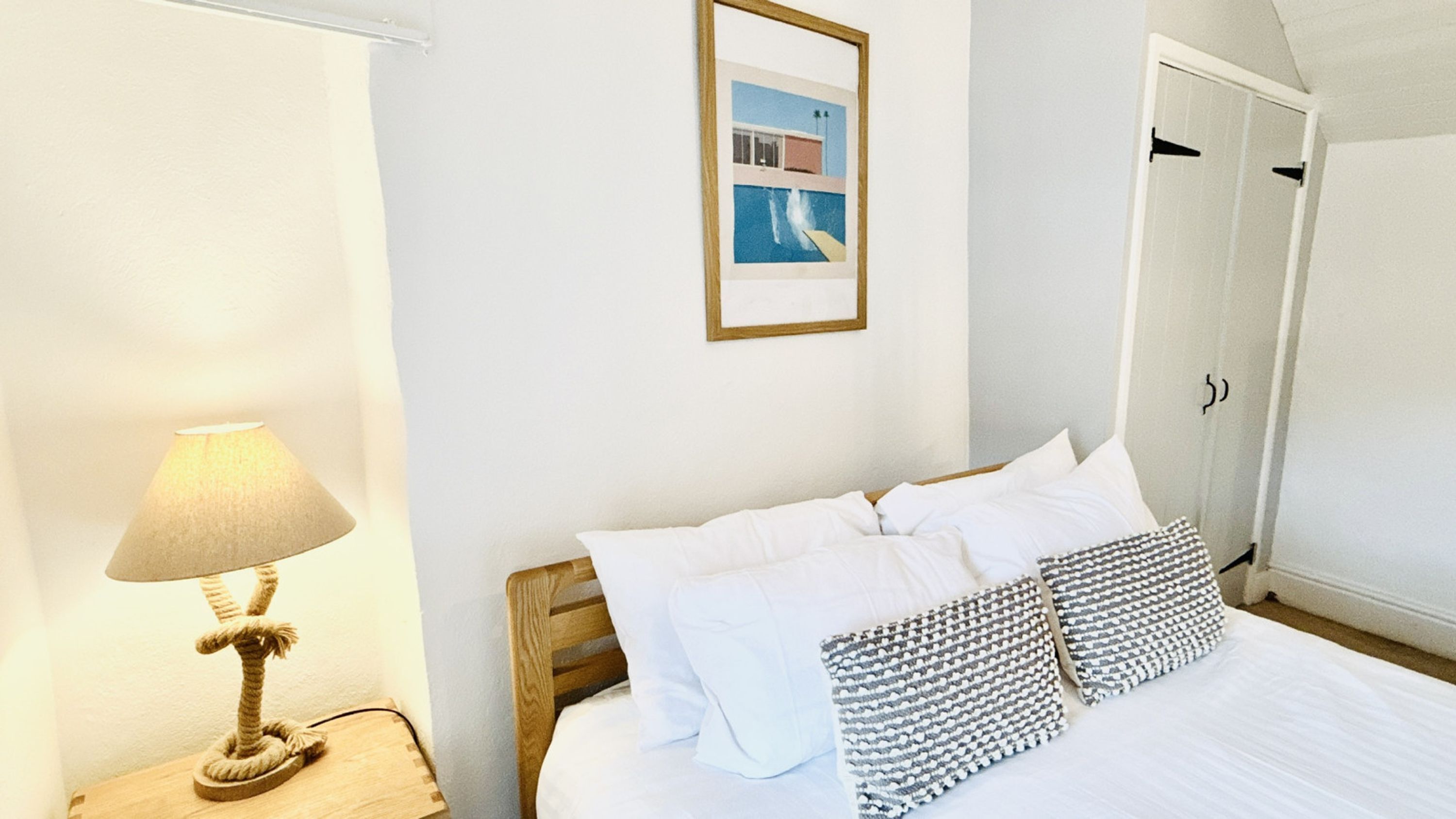 A neatly made bed with white bedding and two patterned pillows, a bedside lamp, and a framed picture on the wall.