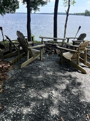 A lakeside seating area with Adirondack chairs and a fire pit. - Charming Lakefront Cabin Rental with a Fire Pit near Brownville, Maine (Brownville)