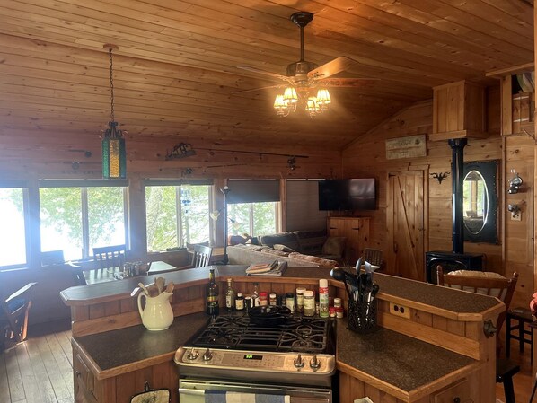 A wooden cabin interior with a kitchen, dining area, and a television.