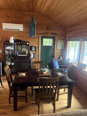 A wooden interior with a dining table, chairs, a vintage radio, and a green door. - Charming Lakefront Cabin Rental with a Fire Pit near Brownville, Maine (Brownville)