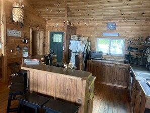 A wooden cabin interior with a kitchen area, bar counter, and seating.