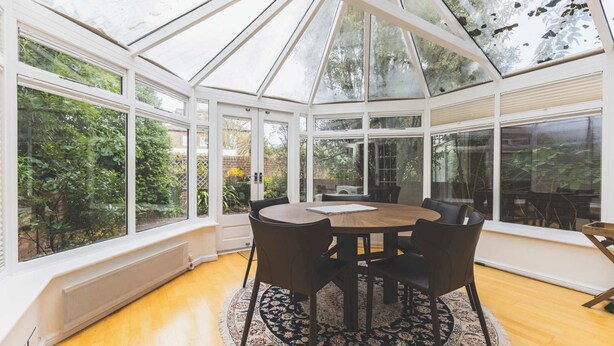 A conservatory with a round table and chairs, large windows, and a view of greenery. - Luxury 3BDR Home w Garden and Parking West London (Greater London)