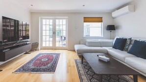 A living room with a sofa, a coffee table, a TV, and a patterned rug. - Luxury 3BDR Home w Garden and Parking West London (Greater London)
