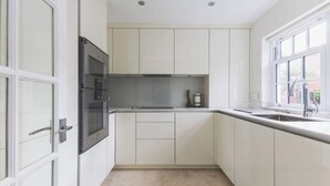 A modern kitchen with white cabinets, a built-in oven, and a window providing natural light. - Luxury 3BDR Home w Garden and Parking West London (Greater London)