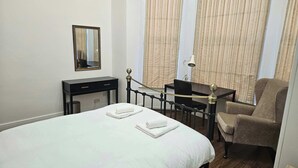 A hotel room with a bed, a desk, a chair, a lamp, and a mirror. - Ground Floor 1BDR Garden Flat South Croydon (Greater London)