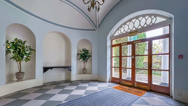 Eine Hotelhalle mit Schachbrettmuster-Boden, Topfpflanzen, einem Chandelier und einem großen Bogenportal.